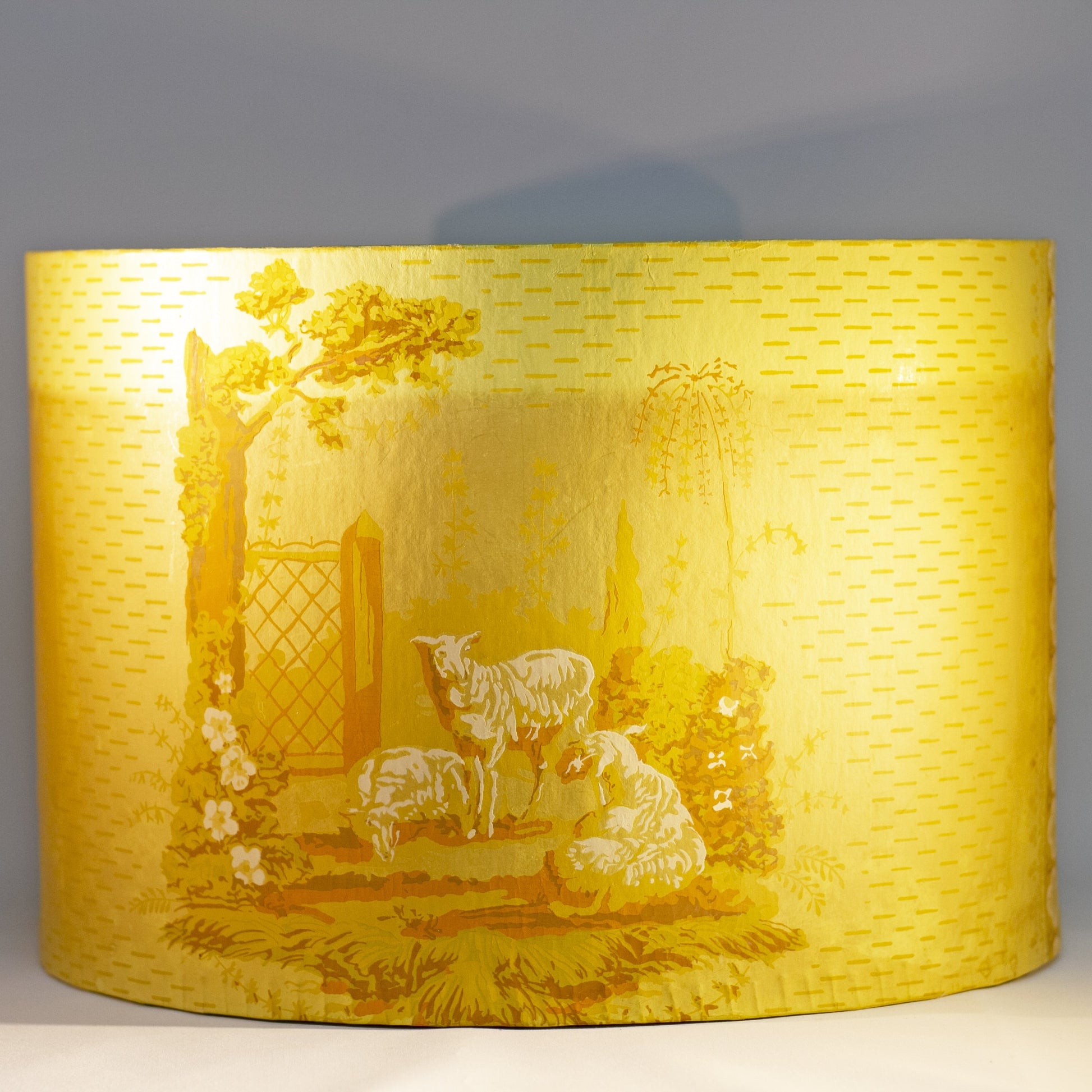 Reproduction of a "BRIDE'S BOX" made from slightly oval shaped large hat box covered in vintage yellow wallpaper featuring lambs and a Colonial girl. Inside and bottom papered with pages from the Maine Antique Digest, September 1977. Measures about 10" high by 15" in length by 13" wide.