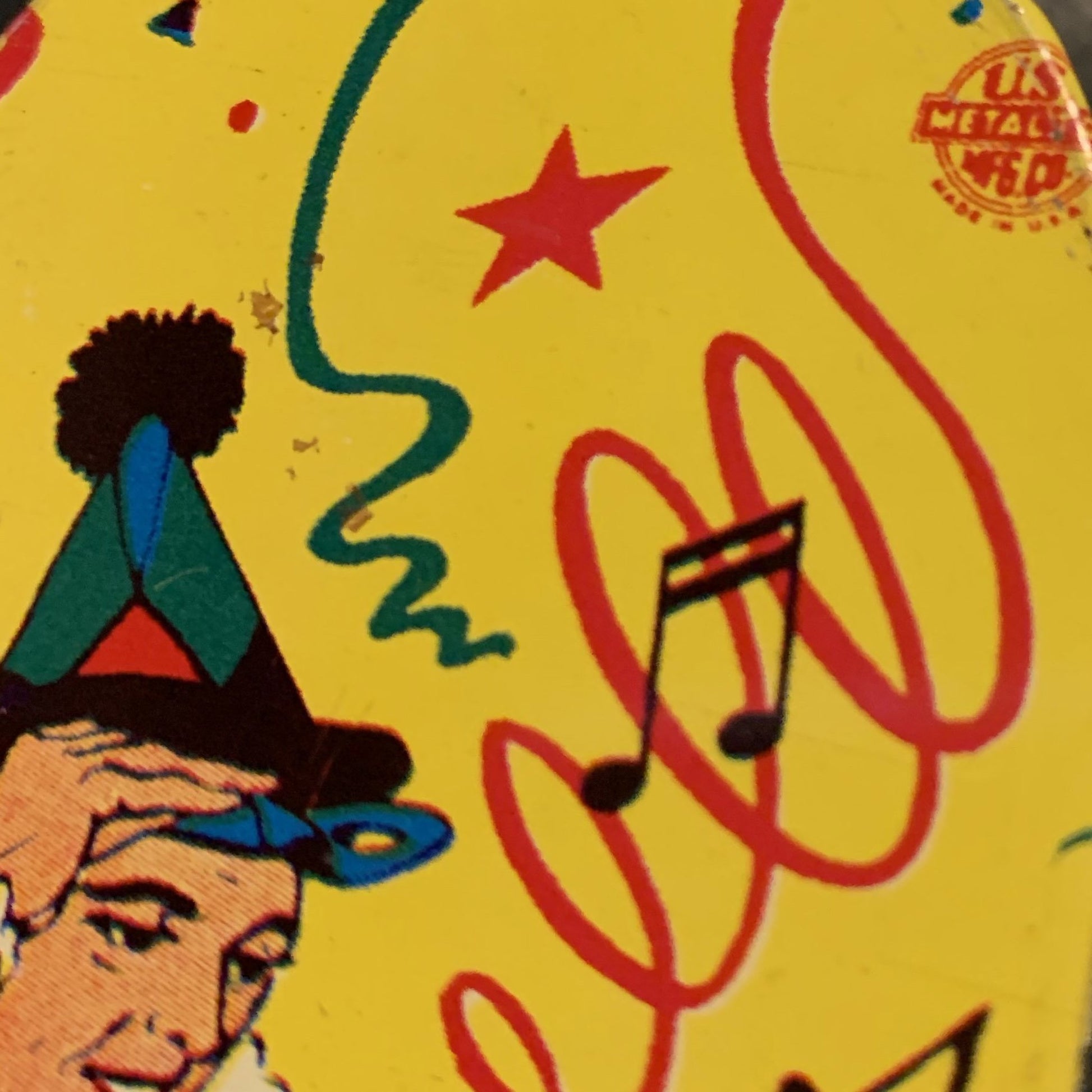 TIN-LITHOGRAPH RATCHET-STYLE MASQUERADE PARTY 1950s NOISEMAKER with green plastic handle by US Metal Toys depicting masquerade dressed couple; the man is dress in a harlequin print jester outfit and the woman in a short cha-cha dress. Lithograph is festive and bright; the background filled with streamers and confetti.