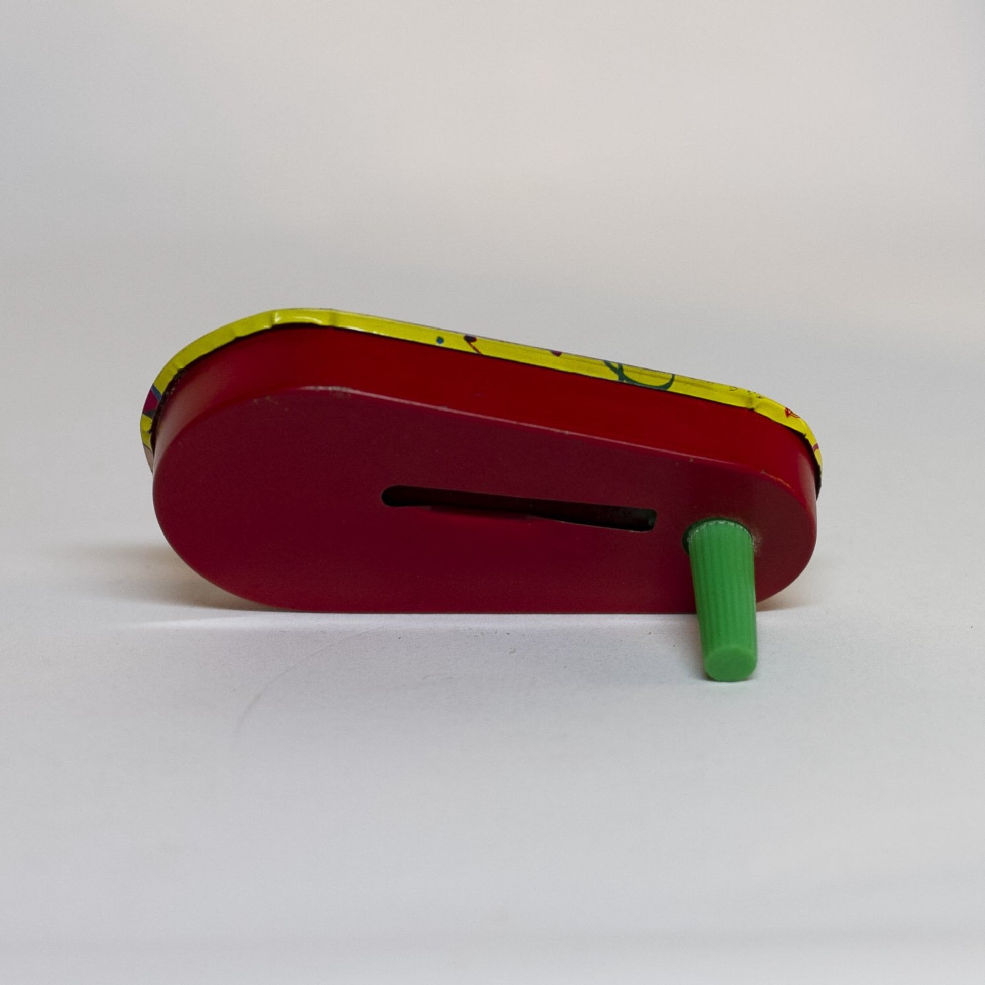 TIN-LITHOGRAPH RATCHET-STYLE MASQUERADE PARTY 1950s NOISEMAKER with green plastic handle by US Metal Toys depicting masquerade dressed couple; the man is dress in a harlequin print jester outfit and the woman in a short cha-cha dress. Lithograph is festive and bright; the background filled with streamers and confetti.