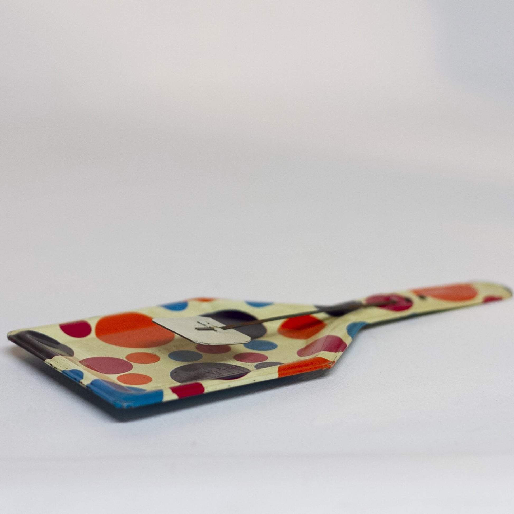 TIN-LITHOGRAPH POLKA DOT CLACKER 1950s NOISEMAKER. The lithograph on the shovel shaped noisemaker is filled with red, orange, purple, and blue polka dots. Appears to be a style that was part of a Party Time set made by the U.S. Metal Toy Manufacturing Company of Brooklyn, New York, but the lithograph is not marked.