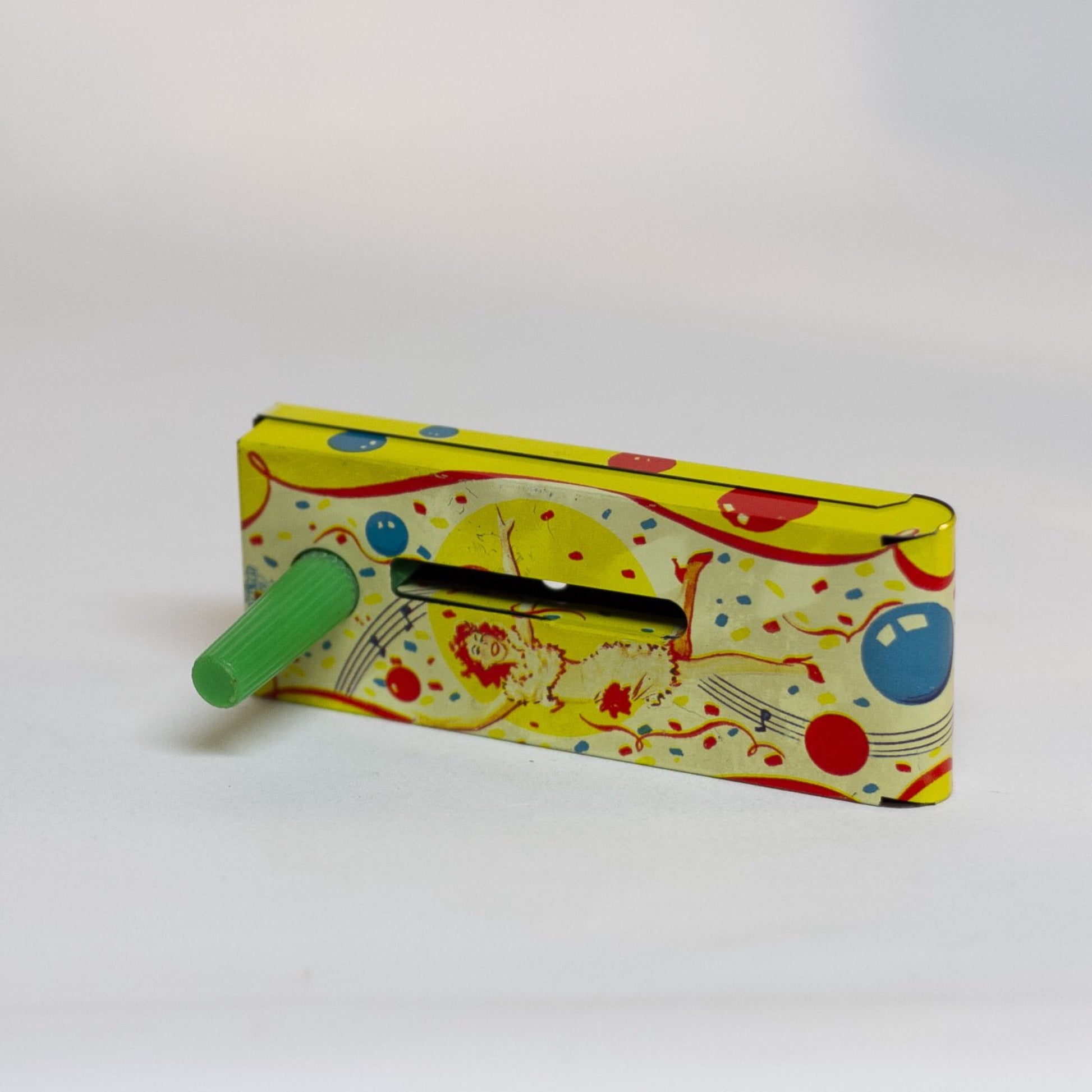 TIN-LITHOGRAPH RATCHET-STYLE JAZZY MUSICIAN NOISEMAKER made by US Metal Toys Mfg from 1950s depicts a jazz musician on front and a red haired woman dancing on the back. The background is filled with festive blue and orange balloons and wavy musical bars. The ratchet handle is made of green plastic. Great Condition.