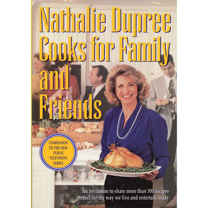 Book cover of 'Nathalie Dupree Cooks for Family and Friends' featuring a smiling Dupree holding a roasted chicken, with large yellow title text over a warm indoor dining scene.