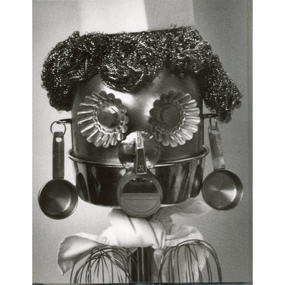 A black and white photograph on the back cover of the cookbook, Second Helpings from Union Square Cafe, of a whimsical, handmade robot or doll made from kitchen utensils, featuring a metal pot for a head with textured hair, flower-shaped eyes, hanging measuring cups, and wire whiskers.