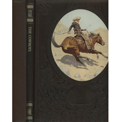 Vintage hardcover book titled "The Cowboys" with a dark brown embossed cover and spine, featuring an oval illustration of a cowboy riding a brown horse across a desert landscape.