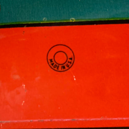 This is an older style tin LITHOGRAPH CLOWN NOISEMAKER that likely dates to the 1930s or 1940s is in the shape of a small can. The lithograph depicts two clowns, one dressed in a white and red polka-dot clown suit and the other is "toothless" and dressed in blue plaid. Scene background in yellow. A red wooden handle is