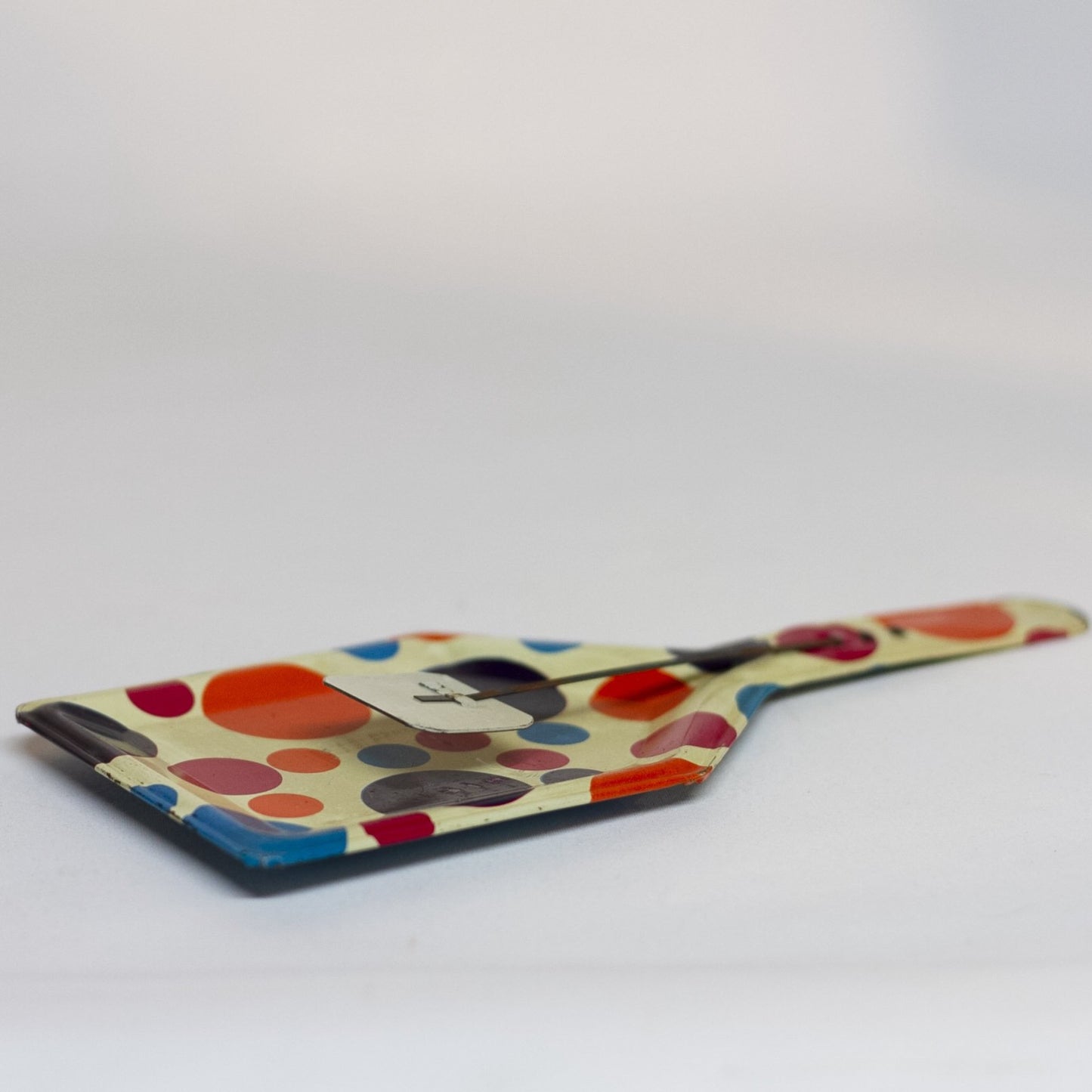 TIN-LITHOGRAPH POLKA DOT CLACKER 1950s NOISEMAKER. The lithograph on the shovel shaped noisemaker is filled with red, orange, purple, and blue polka dots. Appears to be a style that was part of a Party Time set made by the U.S. Metal Toy Manufacturing Company of Brooklyn, New York, but the lithograph is not marked. 